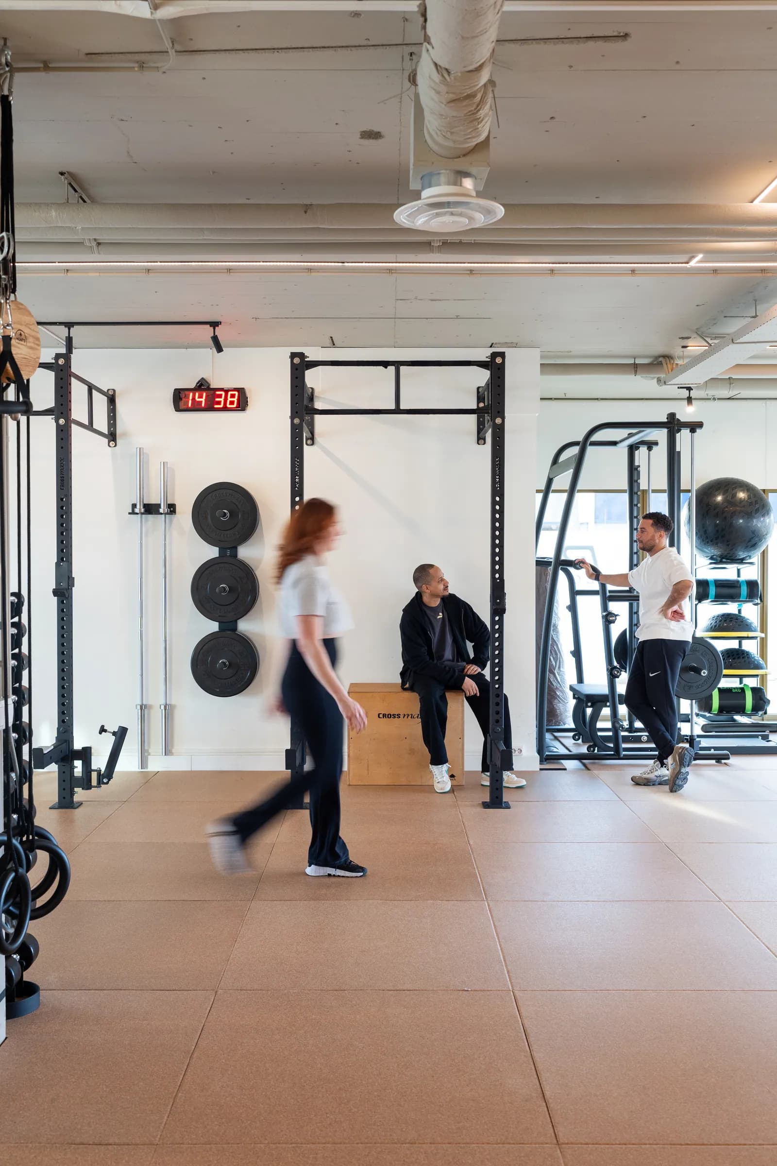 Brede gymzaal met drie personen bij rack en kabels