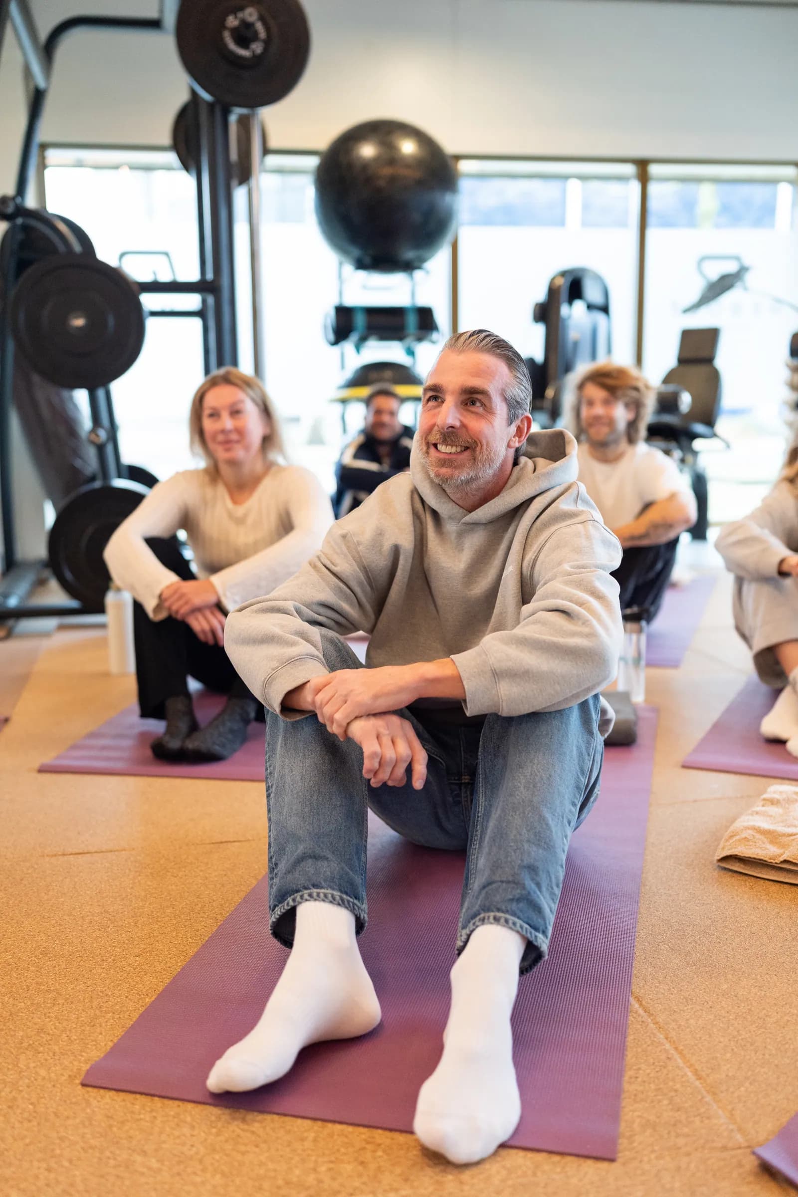 Deelnemer glimlacht op yogamat tijdens groepsessie in lichte gym.