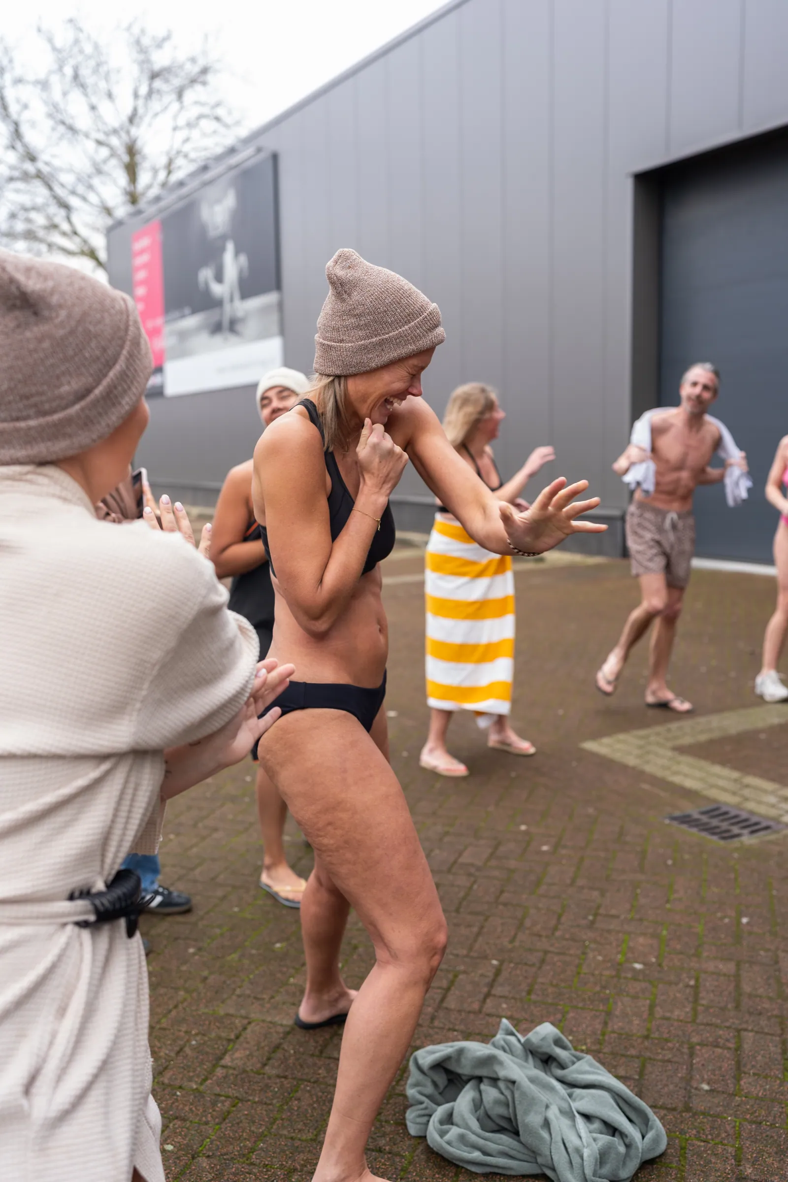 Lachende vrouw in bikini en muts midden in groep na koude training buiten.