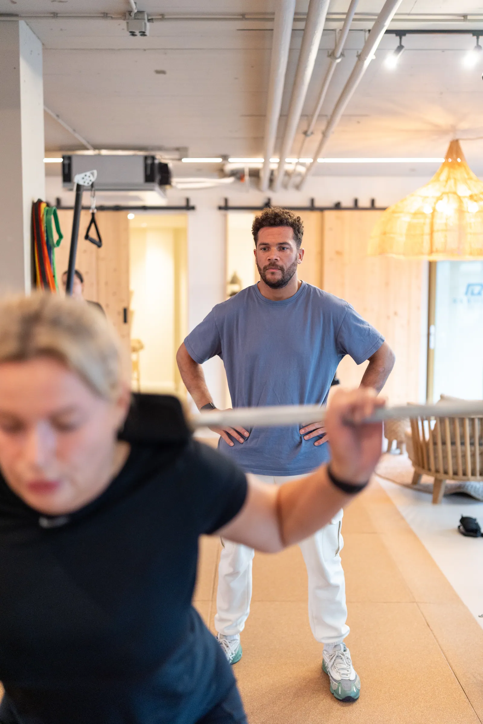 Coach scherp op achtergrond; wazige atlete met barbell op schouders op voorgrond.